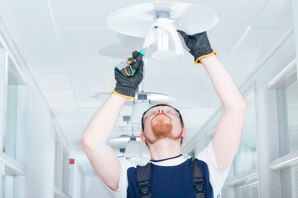 Person wearing protective glasses and gloves working on a broken ceiling light