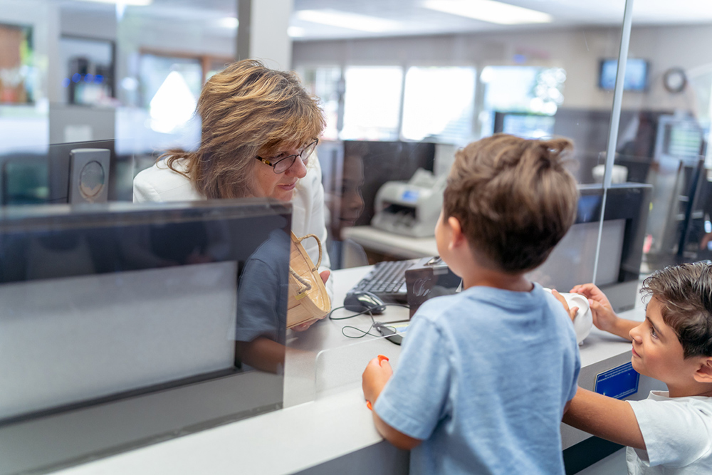 Receptionist behind glass counter speaking to young children