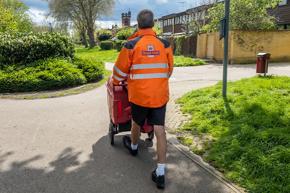 Postperson in uniform walking with post trolley