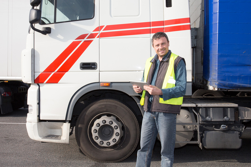 Person wearing high visability jacket and holding a tablet, standing next to a heavy goods vehicle