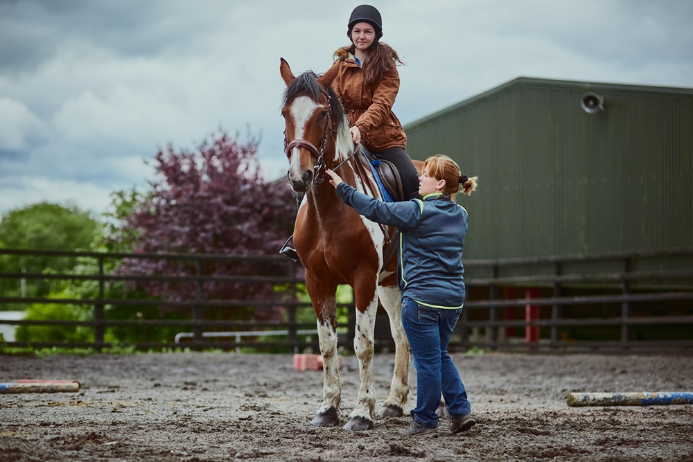 Horse trainer helping a person on a horse