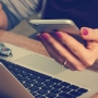 Person's hand using a phone and laptop